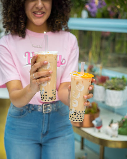 A girl in pink holding two cups of bubble tea half-filled with black tapioca pearls.