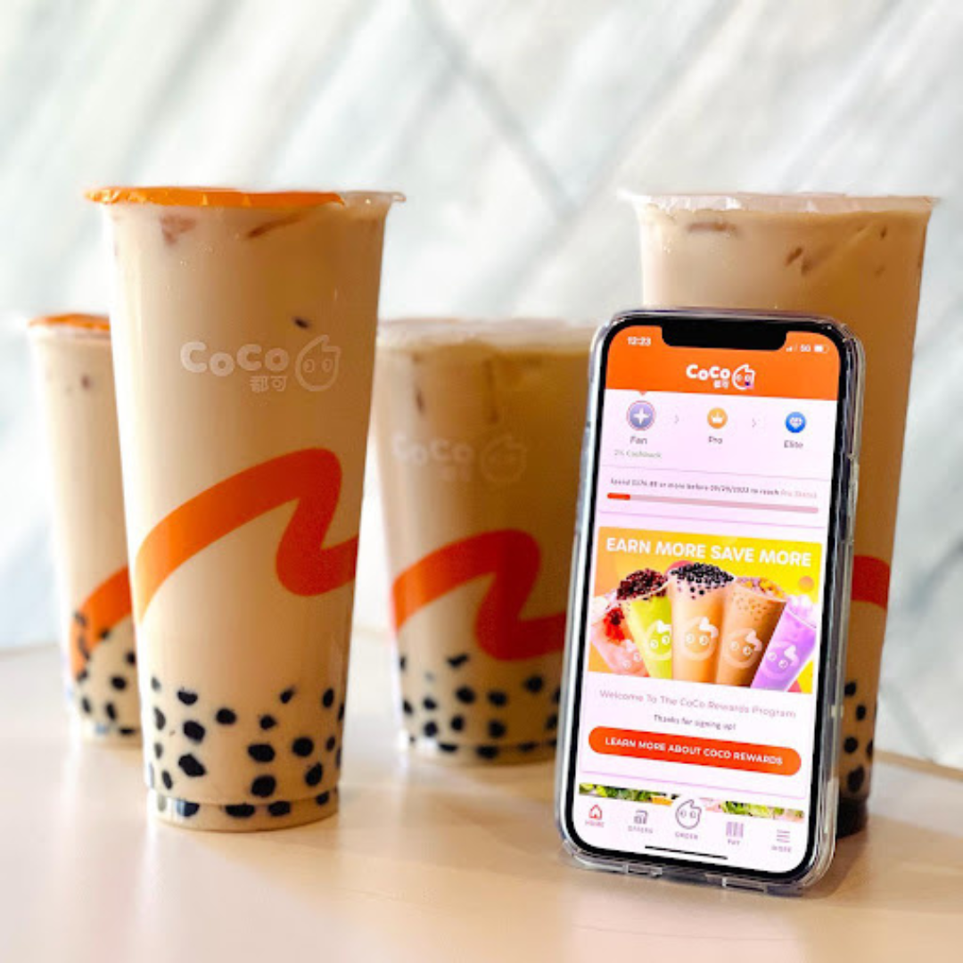 Four cups of CoCo boba tea drinks placed on a table with a cellphone displaying the CoCo boba tea App.