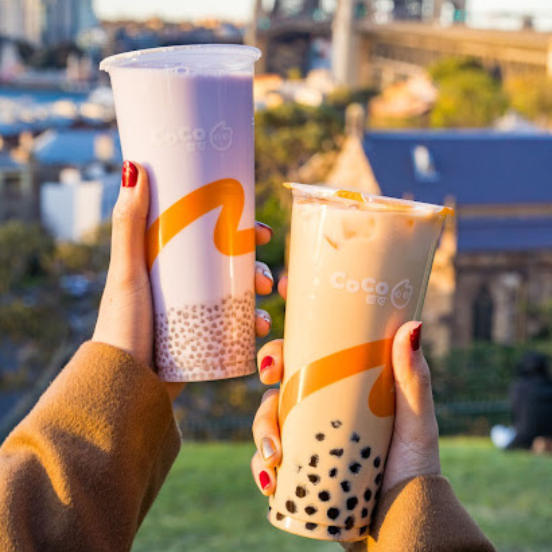 Image of a woman holding two types of boba tea on the grassland.