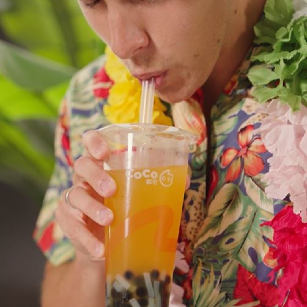 A man in a flowery shirt sipping a cup of CoCo boba tea drink.