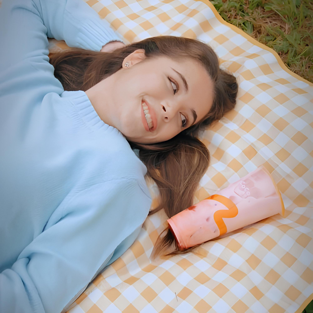 A girl lying on an orange blanket gazing at a cup of CoCo boba tea drink.