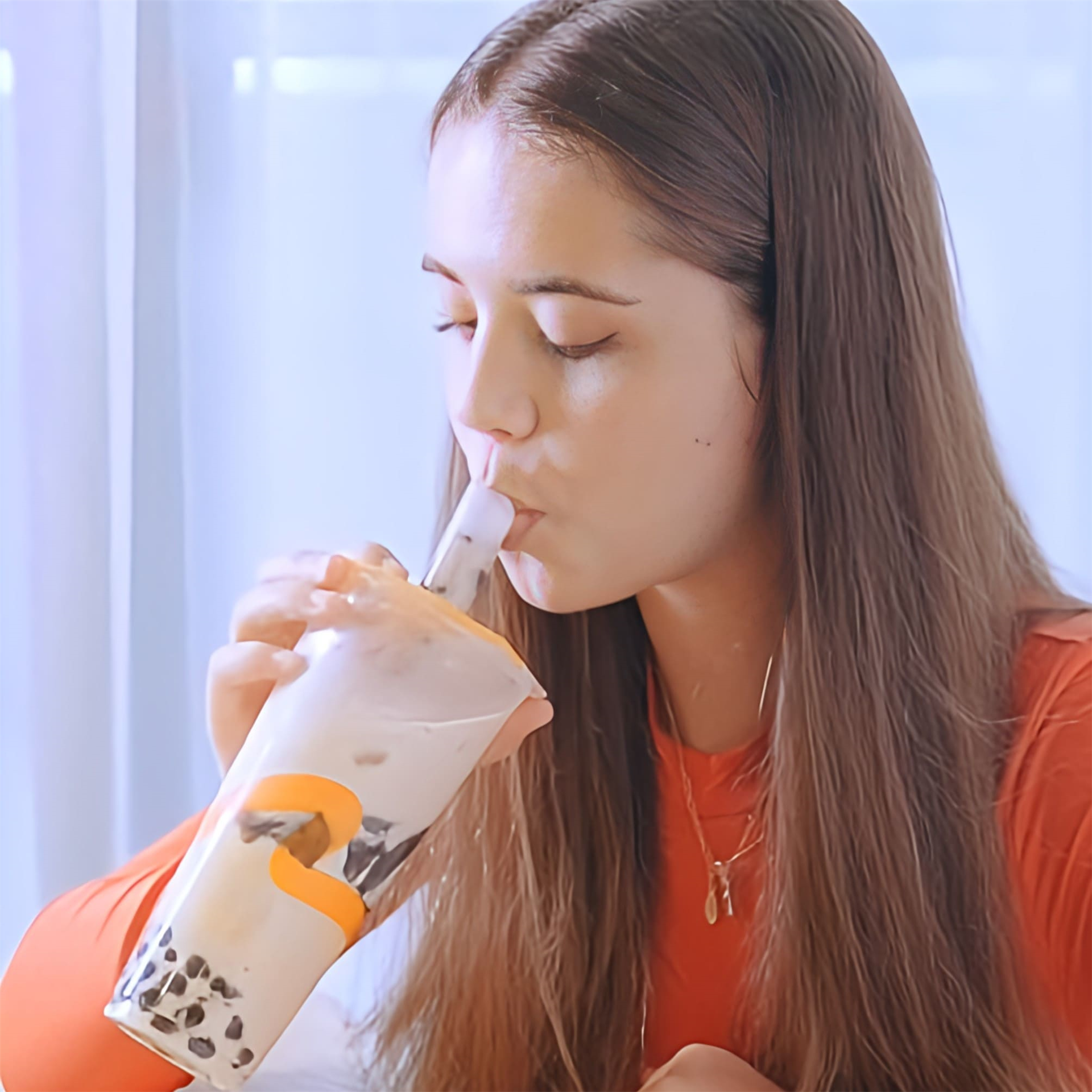 A girl in orange savoring boba tea drink.