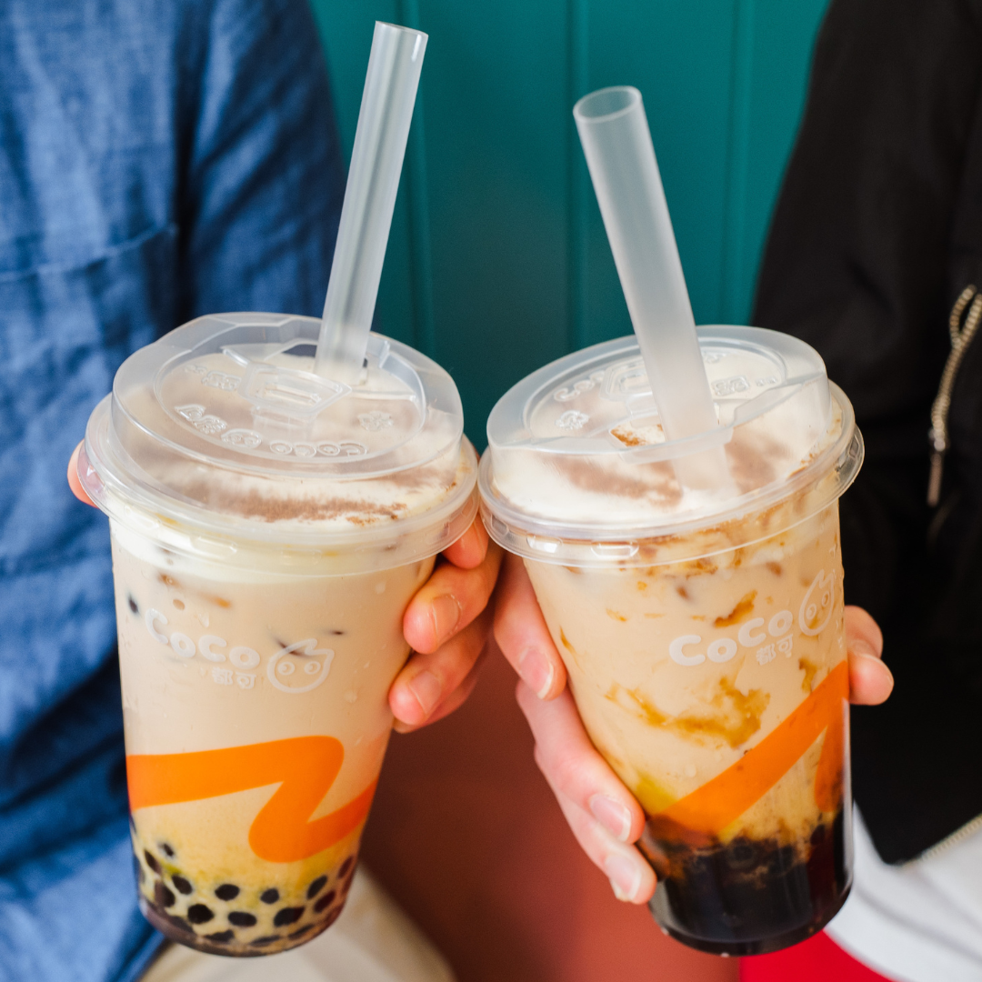 Someone in a blue shirt holding two cups of CoCo bubble tea drinks.